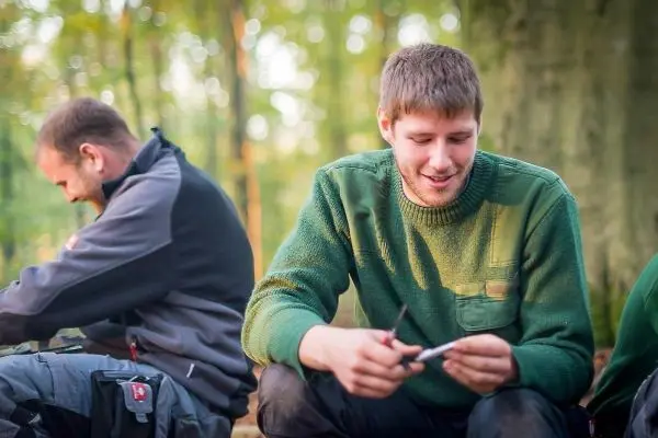 Zwei Personen sitzen im Wald und beschäftigen sich mit Werkzeugen