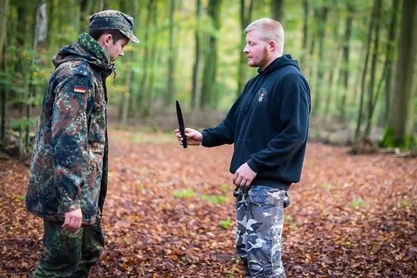 Zwei Personen stehen im Wald, einer hält ein Messer in der Hand