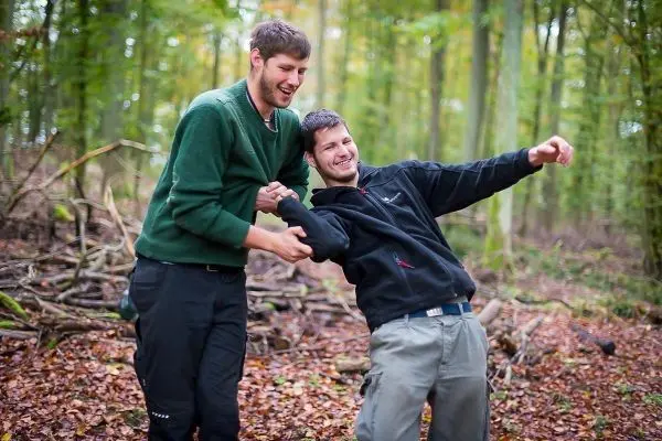 Zwei Personen stehen im Wald und interagieren spielerisch miteinander