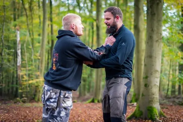 Zwei Personen stehen sich gegenüber und üben eine Nahkampftechnik im Wald aus