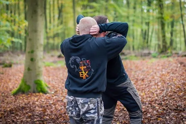 Zwei Personen üben eine Selbstverteidigungstechnik im Wald auf Laubboden