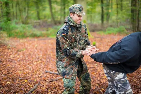 Zwei Personen üben eine Technik zur Handhabung in einem herbstlichen Waldgebiet
