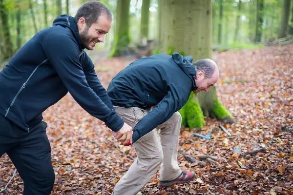 Zwei Personen ziehen an einem Seil im Wald über Laub