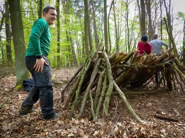 Drei Personen bauen eine Holzunterkunft aus Ästen im Wald