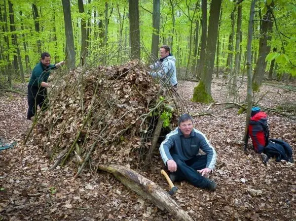Drei Personen bauen eine Laubhütte aus Ästen und Blättern im Wald