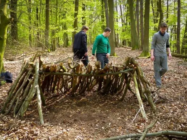 Drei Personen inspizieren eine selbstgebaute Holzstruktur im Wald