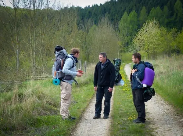 Drei Personen mit Rucksäcken stehen auf einem Waldweg und diskutieren