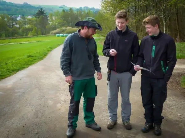 Drei Personen stehen auf einem Weg und betrachten ein Blatt Papier