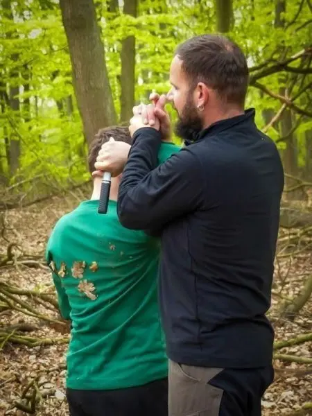 Ein Mann demonstriert eine Technik zur Kontrolle eines anderen im Wald