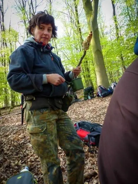 Frau hält einen Stock mit einem Topf über dem Boden in einem Wald