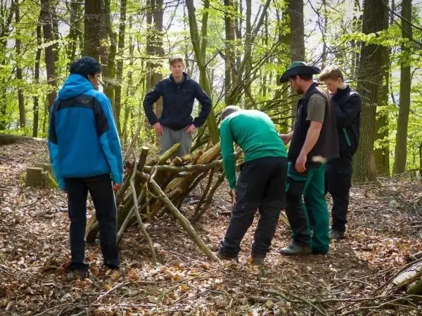 Gruppe arbeitet an einer selbstgebauten Unterkunft im Wald beim Survival Training