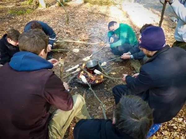 Gruppe sitzt um ein Feuer und röstet Stockbrot beim Überlebenstraining