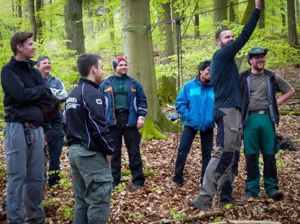 Gruppe steht im Wald und beobachtet eine Demonstration zur Seilquerung