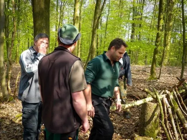 Gruppe von Personen steht im Wald neben einer selbstgebauten Konstruktion aus Ästen