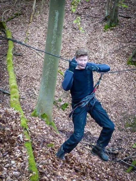Junge überquert selbstgebaute Seilbrücke zwischen Bäumen im Laubwald