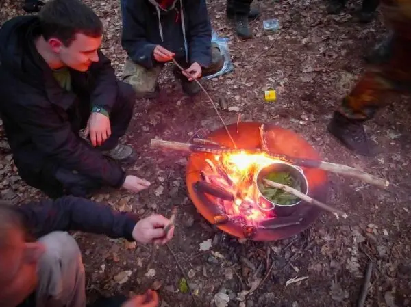 Kessel über offenem Feuer mit Gemüse, Teilnehmer halten Stöcke in der Nähe