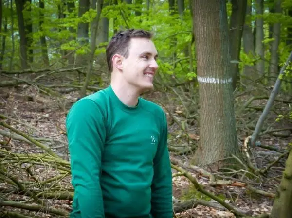 Lächelnder Mann in grünem Oberteil sitzt im Wald zwischen Ästen und Bäumen