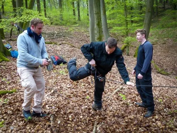 Mann balanciert auf einem Seil, während zwei andere ihn unterstützen