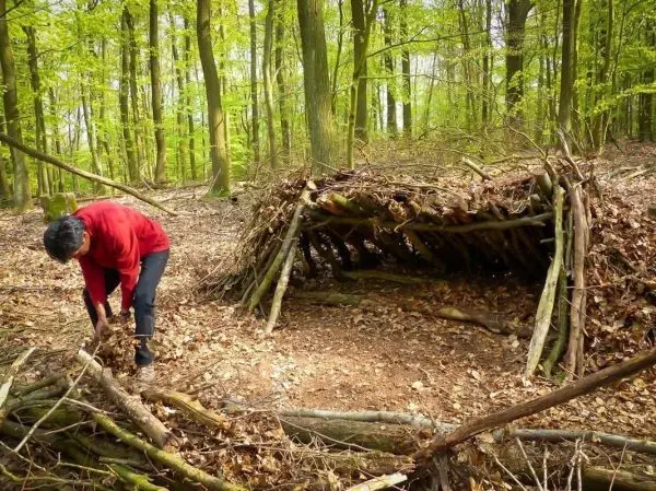 Mann baut eine Laubhütte aus Ästen und Blättern im Wald