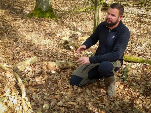 Mann erklärt eine selbstgebaute Schlagfalle im Laubwald