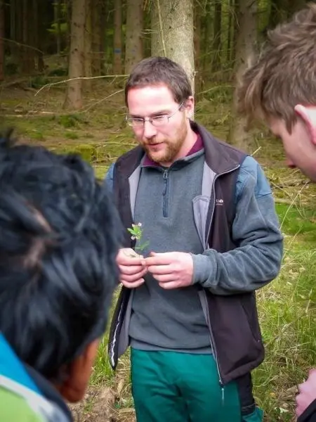 Mann hält eine Pflanze in der Hand und erklärt sie einer Gruppe im Wald