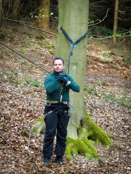 Mann in Kletterausrüstung nutzt Seil zur Baumquerung