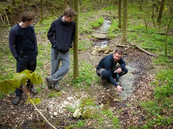 Mann kniet neben einem kleinen Wasserlauf und untersucht das Wasser