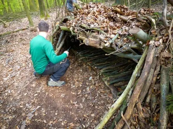Mann überprüft eine selbstgebaute Laubhütte aus Ästen und Blättern