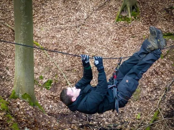 Mann überquert eine selbstgebaute Seilbrücke zwischen zwei Bäumen