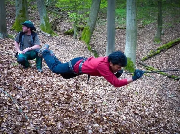 Mann überquert mit Seil eine schräge Fläche im Wald