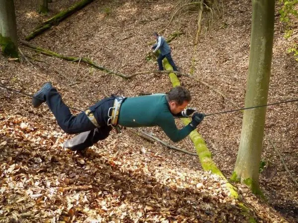Mann überquert mit Seil eine steile, mit Laub bedeckte Abhänge