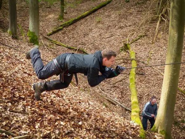Mann überquert selbstgebaute Seilbrücke zwischen Bäumen im Laubwald
