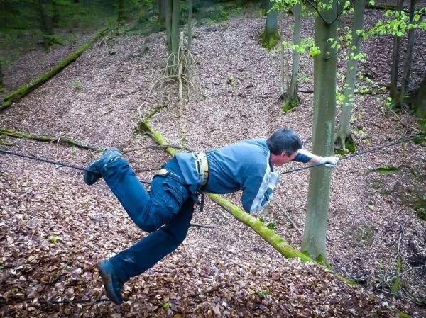 Mann überquert selbstgebaute Seilbrücke zwischen zwei Bäumen