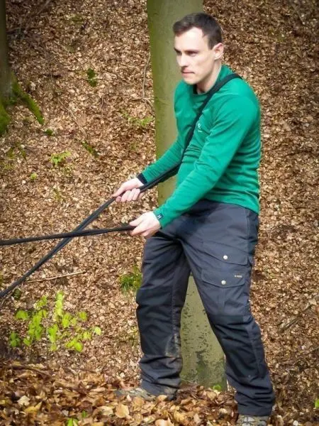 Mann zieht an einem Seil in einem Waldgebiet mit Laubboden