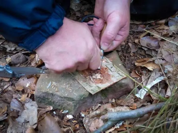 Person bearbeitet ein Stück Papier auf einem Stein