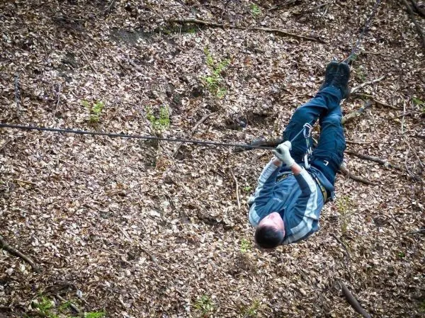 Person hängt an einem Seil über Laubboden beim Überlebenstraining