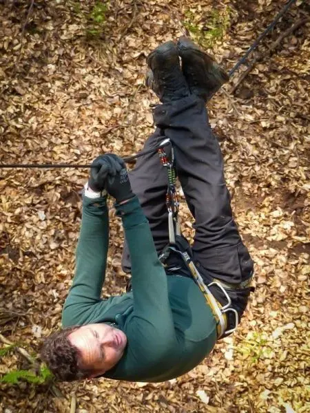 Person hängt kopfüber an einem Seil im Laubwald