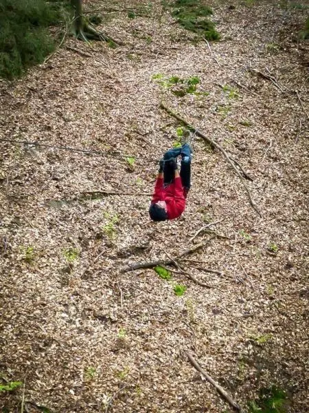 Person hängt kopfüber an einem Seil über Laubboden