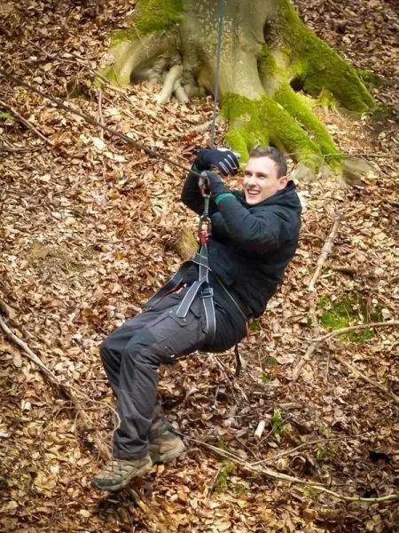 Person schwingt an einem Seil über den Boden im Wald