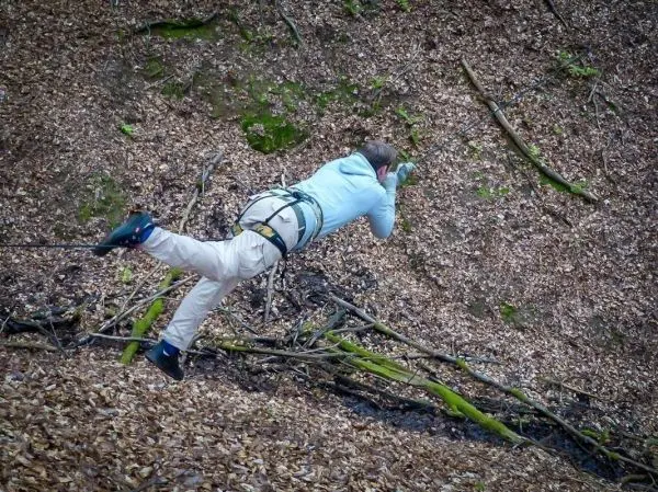 Person schwingt an Seil über den Boden im Wald