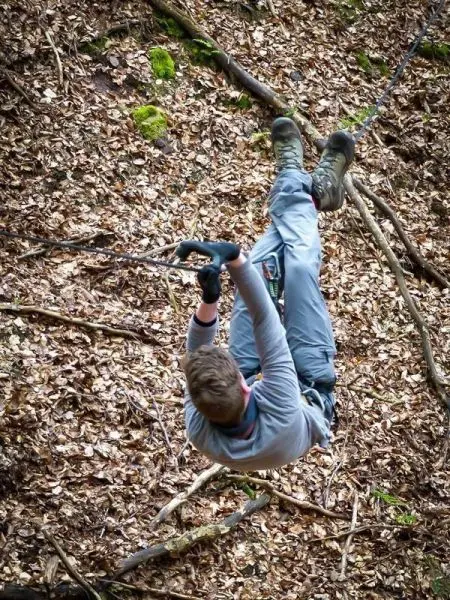 Person schwingt an Seil über den Boden im Wald