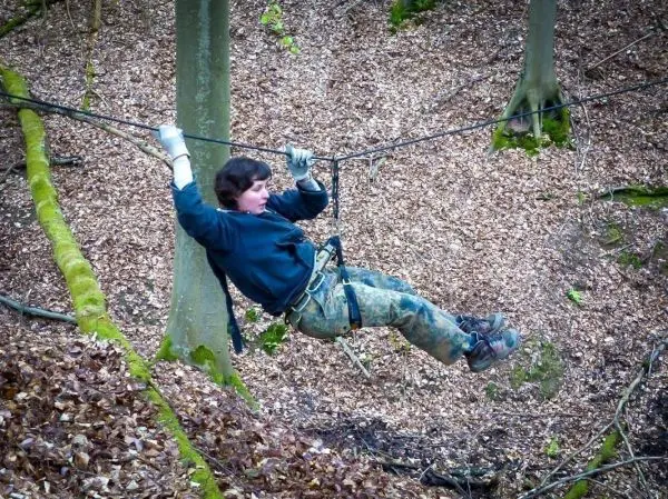 Person schwingt an Seil zwischen Bäumen im Laubwald beim Überlebenstraining