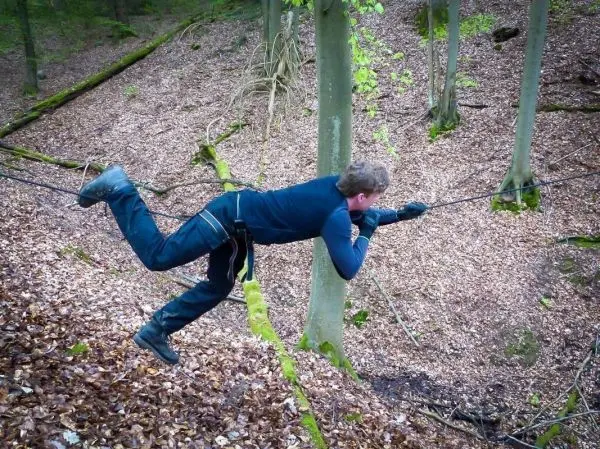 Person schwingt an selbstgebauter Seilbrücke zwischen Bäumen