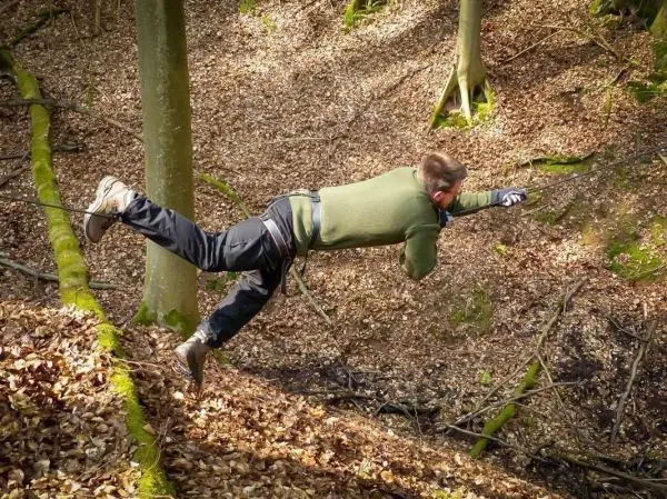 Person springt über einen Abhang im Wald beim Survival Training