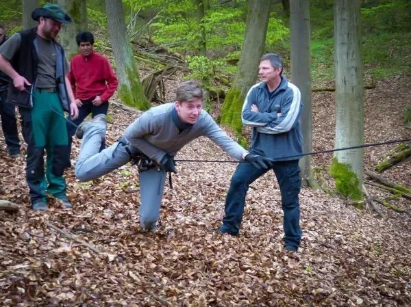 Person zieht an Seil, während andere zuschauen im Wald beim Überlebenstraining