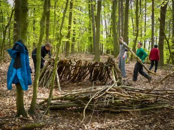 Personen bauen eine Unterkunft aus Ästen im Wald beim Survival Training