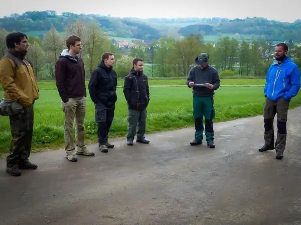 Sechs Personen stehen auf einem Weg und hören einem Mann mit Notizen zu