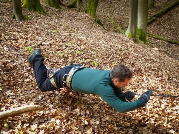 Seilquerung über Laubboden mit gesichertem Gurtzeug und Handschuhen