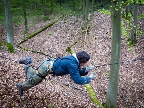 Seilquerung über Laubboden mit gesichertem Klettergurt und Handschuhen