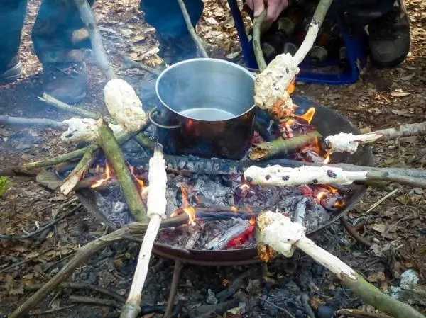 Töpfe stehen über einem Feuer, während Brot auf Stöcken geröstet wird